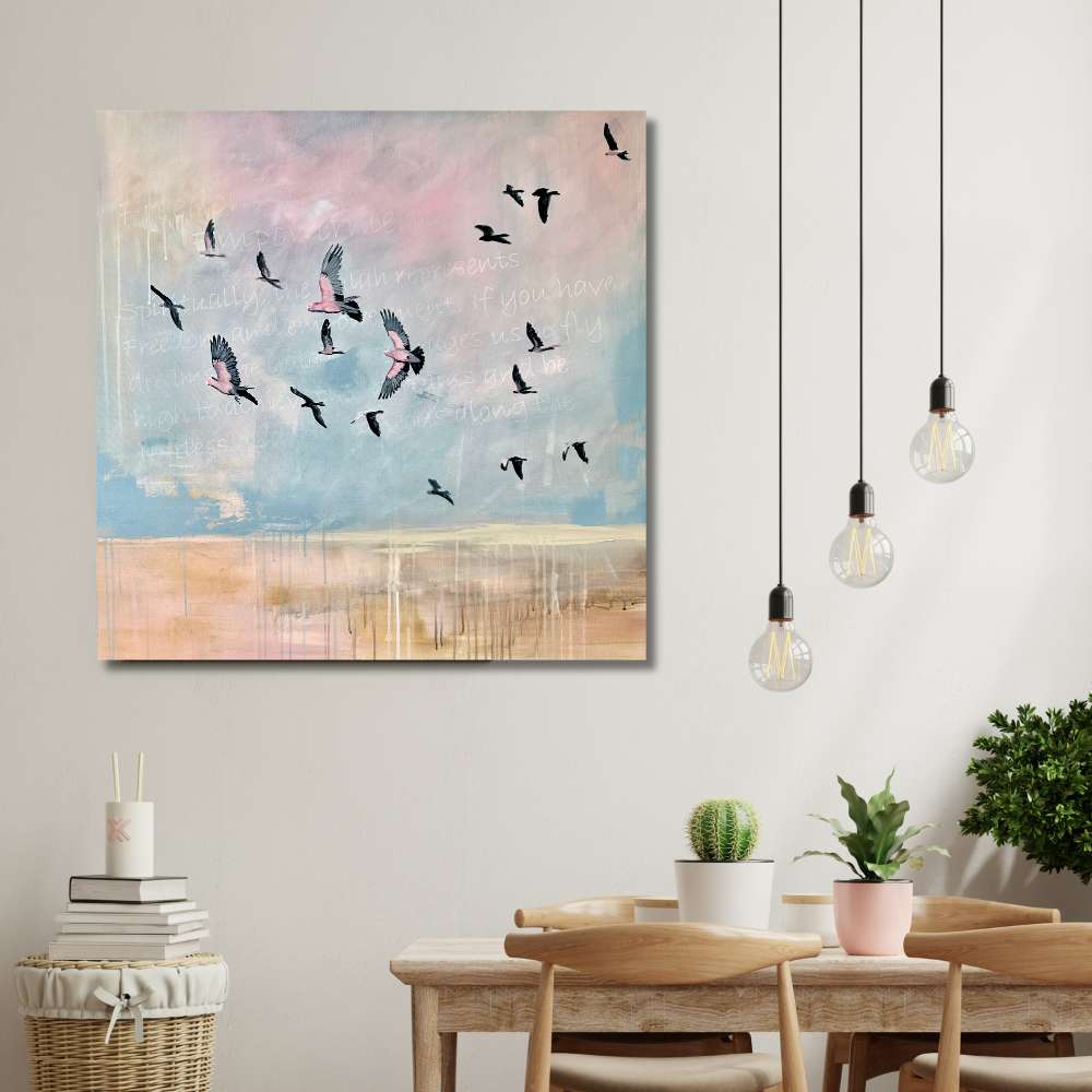 An abstract canvas wall art print depicting birds flying across a pastel sky, displayed in a modern dining room setting above a wooden table with chairs and hanging pendant lights.